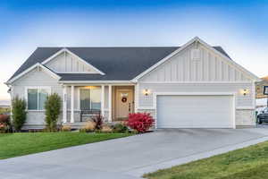 View of front of property with board and batten siding, covered porch, a front lawn, concrete driveway, and an attached garage