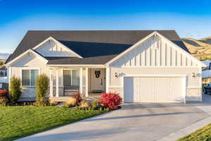View of front of house with covered porch, board and batten siding, a front yard, concrete driveway, and roof with shingles