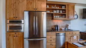 Kitchen with stainless steel appliances, open shelves, decorative backsplash, and dark stone counters