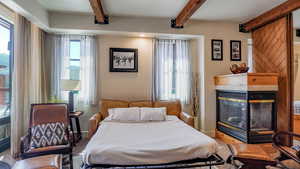 Carpeted bedroom featuring a tiled fireplace and beamed ceiling