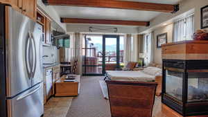 Bedroom with freestanding refrigerator, a fireplace, beam ceiling, multiple windows, and access to exterior