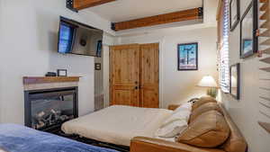Bedroom featuring a glass covered fireplace, beamed ceiling, and a closet