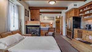 Bedroom featuring beam ceiling, freestanding refrigerator, a fireplace, and light tile patterned floors