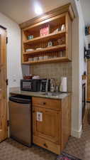 Bar area with decorative backsplash, open shelves, light stone counters, black microwave, and a glass covered fireplace