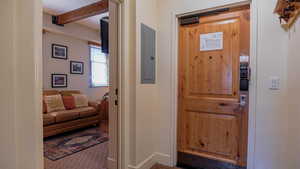 Hallway with electric panel, carpet flooring, and beam ceiling