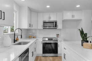 Kitchen with white cabinets, appliances with stainless steel finishes, light stone counters, tasteful backsplash, and recessed lighting