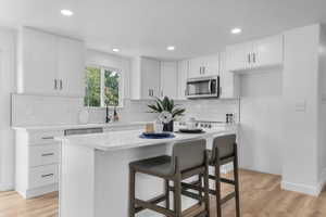 Kitchen featuring light wood-type flooring, a breakfast bar area, white cabinets, a kitchen island, and tasteful backsplash