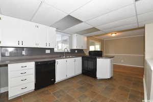 Kitchen with dark countertops, black appliances, white cabinets, a drop ceiling, and a peninsula