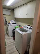 Washroom featuring light wood-type flooring, cabinet space, and independent washer and dryer