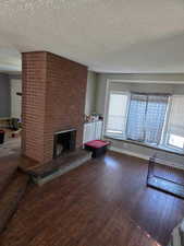Unfurnished living room with a fireplace, dark wood finished floors, and a textured ceiling