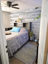 Bedroom featuring wooden walls, a ceiling fan, and a textured ceiling
