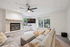 Living area with carpet, a stone fireplace, a ceiling fan, and recessed lighting
