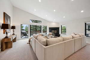 Living area with recessed lighting, light carpet, a fireplace with raised hearth, and high vaulted ceiling