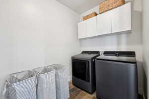 Washroom with cabinet space, dark stone finish flooring, and washing machine and dryer
