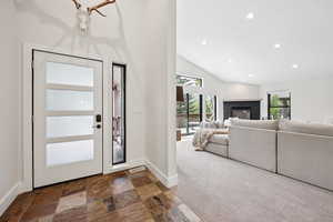 Foyer with recessed lighting, stone tile floors, high vaulted ceiling, dark carpet, and a glass covered fireplace
