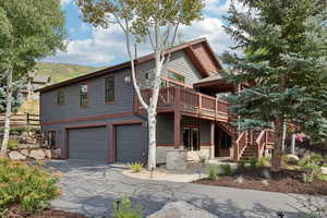 View of front facade featuring a wooden deck, a garage, stairway, and asphalt driveway
