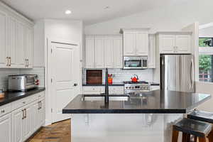 Kitchen featuring stainless steel appliances, lofted ceiling, white cabinets, backsplash, and recessed lighting