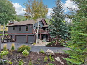 View of front of house featuring an attached garage, driveway, a wooden deck, stairs, and roof with shingles