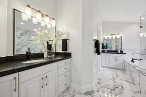 Full bathroom with two vanities, a bath, light marble finish floors, and recessed lighting