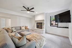 Carpeted living room with ceiling fan, a stone fireplace, and recessed lighting