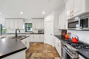 Kitchen with stainless steel appliances, recessed lighting, white cabinetry, dark stone finish floors, and backsplash