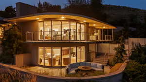 Back of house at night featuring a balcony, an outdoor living space with a fire pit, stucco siding, and stairs
