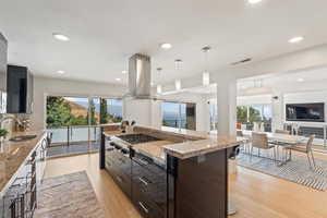 Kitchen with light stone counters, pendant lighting, light wood finished floors, island range hood, and a breakfast bar area