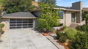 View of side of property with stucco siding, concrete driveway, a garage, a chimney, and a shingled roof