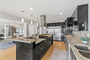 Kitchen with dark cabinets, light stone countertops, pendant lighting, tasteful backsplash, and recessed lighting
