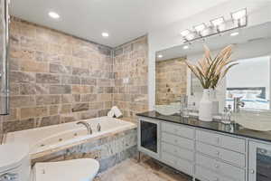 Full bathroom with tile walls, a jetted tub, double vanity, and recessed lighting