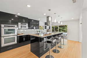 Kitchen featuring dark cabinets, tasteful backsplash, a breakfast bar, pendant lighting, and appliances with stainless steel finishes