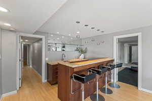 Bar area with wood counters, hanging light fixtures, light wood-style flooring, recessed lighting, and modern cabinets