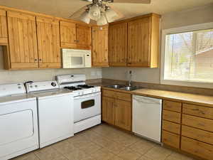 Kitchen featuring white appliances, light tile patterned floors, light countertops, a ceiling fan, and independent washer and dryer
