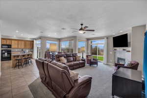 Living area featuring a tile fireplace, ceiling fan, recessed lighting, light tile patterned floors, and light colored carpet