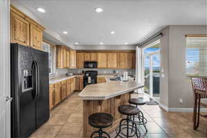 Kitchen featuring black appliances, light countertops, a kitchen breakfast bar, recessed lighting, and light tile patterned floors