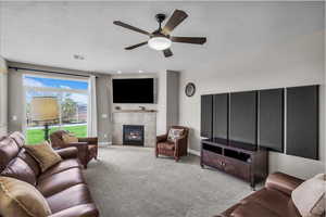 Living room featuring a tile fireplace, carpet floors, a textured ceiling, and ceiling fan