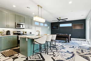 Kitchen with green cabinetry, appliances with stainless steel finishes, a ceiling fan, a kitchen breakfast bar, and a center island with sink