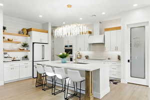 Kitchen with open shelves, both dramatic statement and lighting, white appliances, light countertops, and a breakfast bar