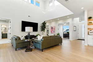 Living room featuring light wood-style flooring, recessed lighting, and a towering ceiling
