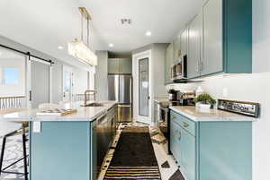 Kitchen with a kitchen island with sink, appliances with stainless steel finishes, a breakfast bar, a barn door, and recessed lighting