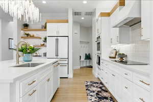 Bright white kitchen featuring open shelves, under cabinet range hood, white appliances, tile backsplash, and white cabinets