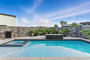 View of swimming pool featuring a fenced backyard and a pool with connected hot tub and water feature.