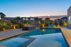 Pool at dusk with a patio, a fenced backyard, and a pool with connected hot tub. there is a water and fire feature not o in this photo.