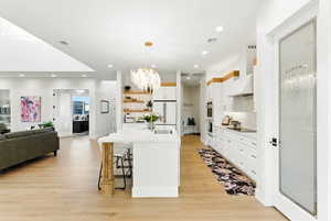 Kitchen with a kitchen bar, a chandelier, white cabinets, dramatic statement hanging light fixtures, and open floor plan