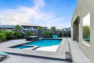 View of swimming pool with a patio, a pool with connected hot tub, and a fenced backyard.