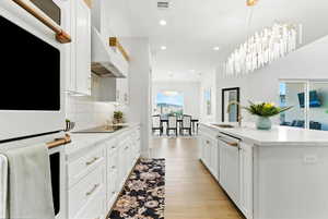Bright kitchen featuring white appliances, tasteful backsplash, recessed lighting, an island with sink, and white cabinetry