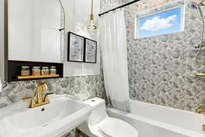 Beautiful full bath featuring shower / bath combination with curtain and wallpapered walls. Did you notice the diamond drop lighting pendant?