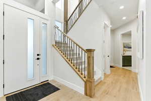 Entrance foyer with light wood-style floors and stunning staircase with dramatic high impact lighting.