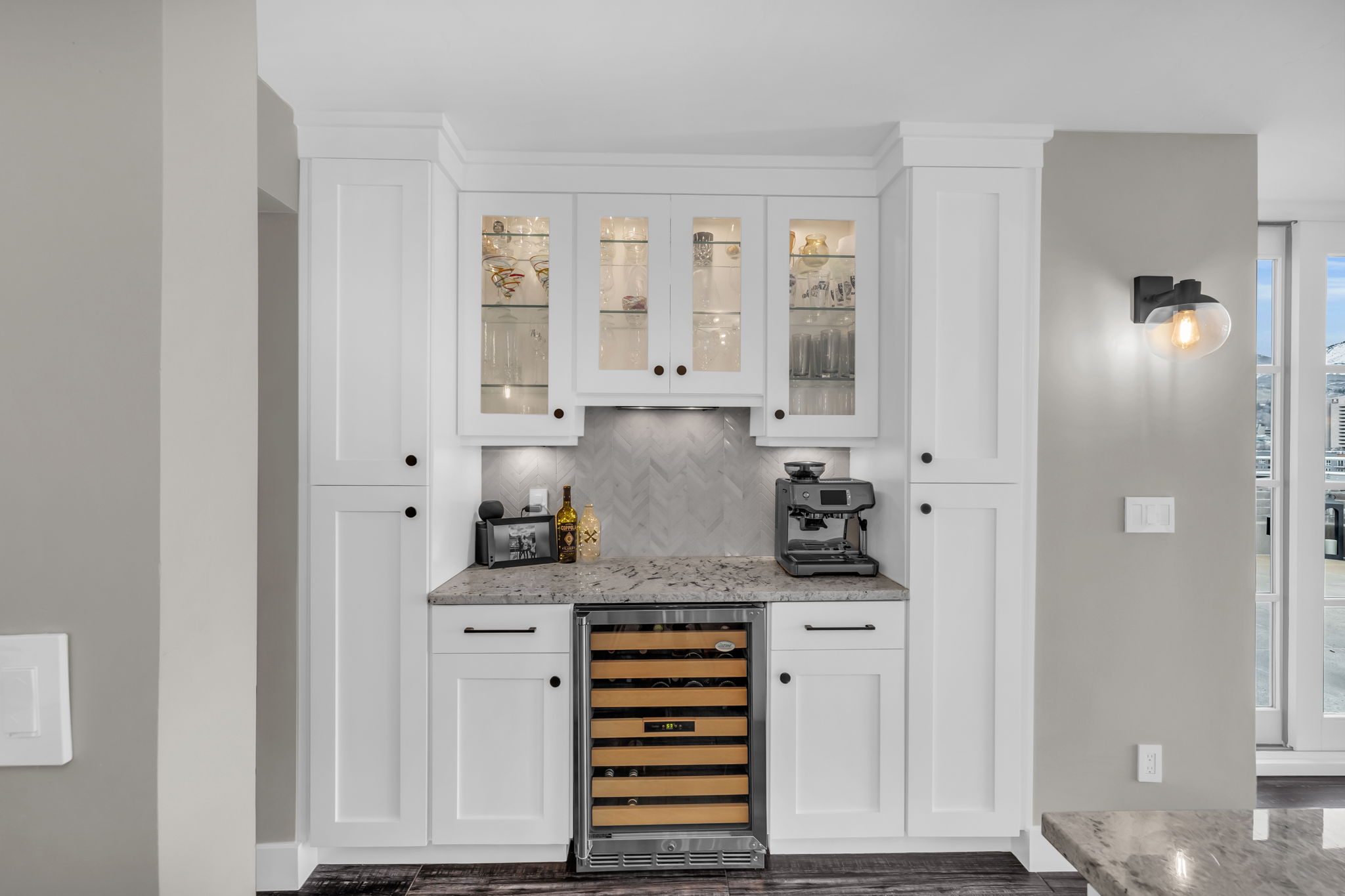 Indoor dry bar featuring wine cooler, decorative backsplash, light stone countertops, white cabinetry, and glass insert cabinets
