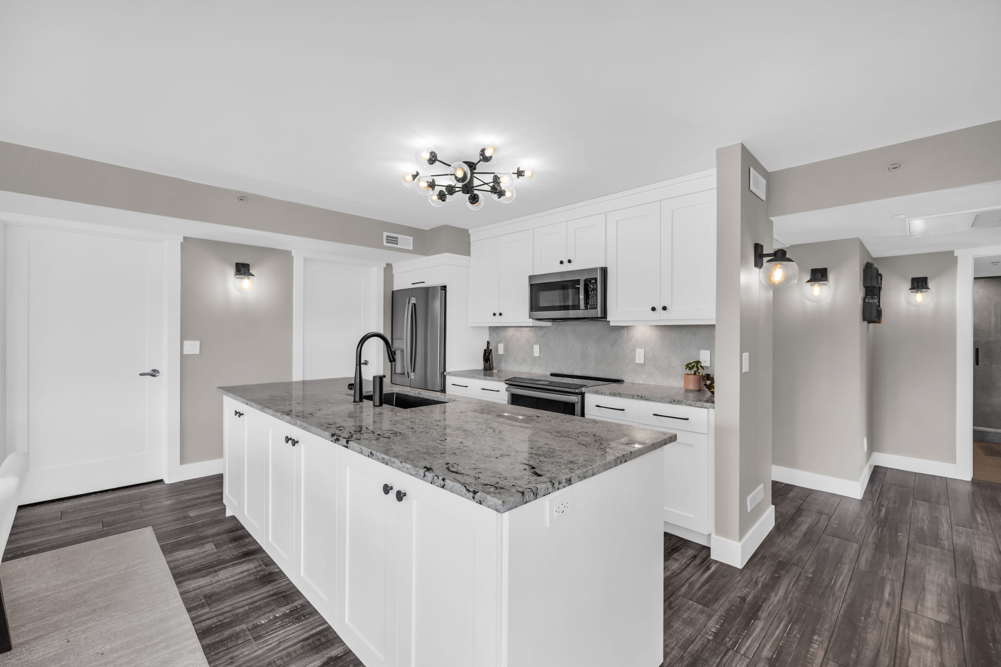 Kitchen featuring light stone counters, white cabinetry, tasteful backsplash, stainless steel appliances, and a kitchen island with sink